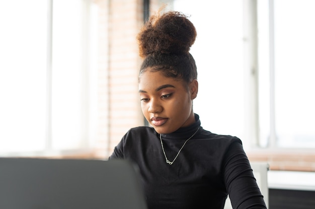 Hermosa joven africana en la mesa con un portátil en la oficina