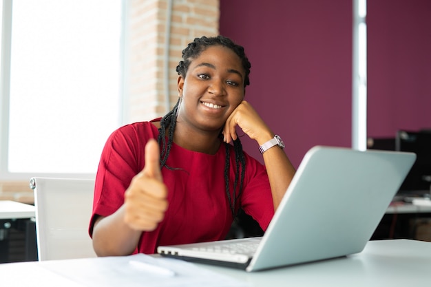 Foto hermosa joven africana en la oficina con un portátil