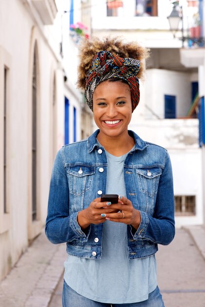 Hermosa joven africana permanente al aire libre con teléfono inteligente