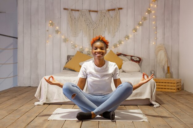 Hermosa joven africana en pose de yoga en casa en el dormitorio