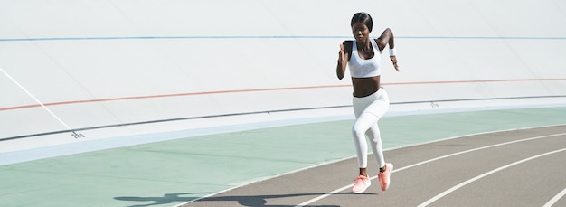 Hermosa joven africana en ropa deportiva corriendo en la pista al aire libre