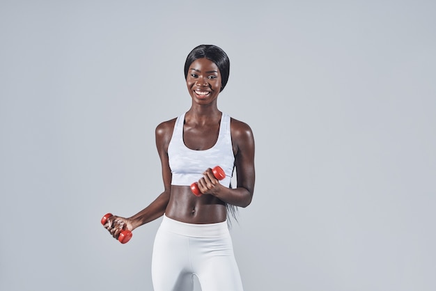 Hermosa joven africana en ropa deportiva haciendo ejercicio con pesas