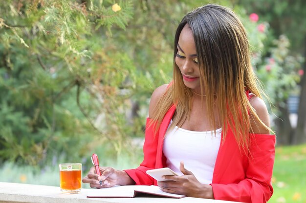 Hermosa joven africana con teléfono y bolígrafo rojo en las manos