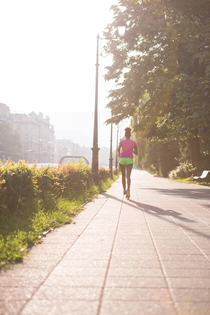 Hermosa joven afroamericana deportiva corriendo temprano en la mañana trotando con la escena del amanecer de la ciudad en el fondo