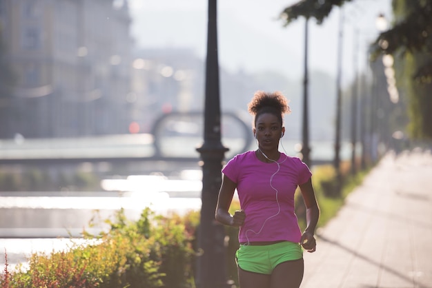 Hermosa joven afroamericana deportiva corriendo temprano en la mañana trotando con la escena del amanecer de la ciudad en el fondo