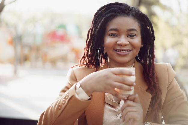 Hermosa joven afroamericana sentada en la cafetería al aire libre y tomando café