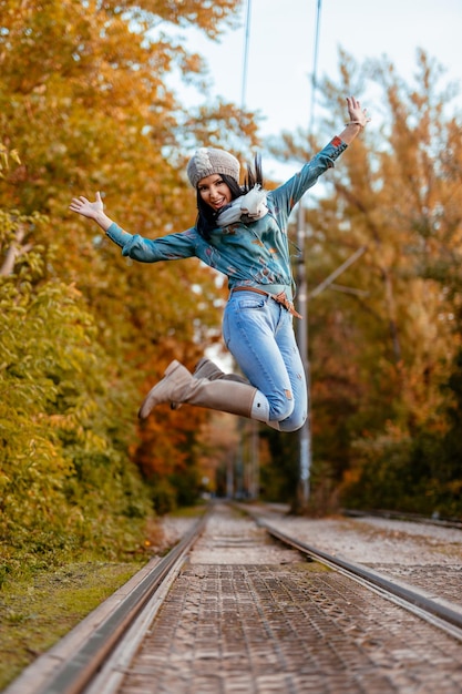 Hermosa joven alegre disfrutando de los colores del otoño saltando en el parque de la ciudad con felicidad.