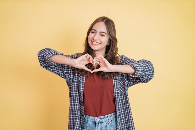 Hermosa joven alegre está gesticulando un corazón con los dedos