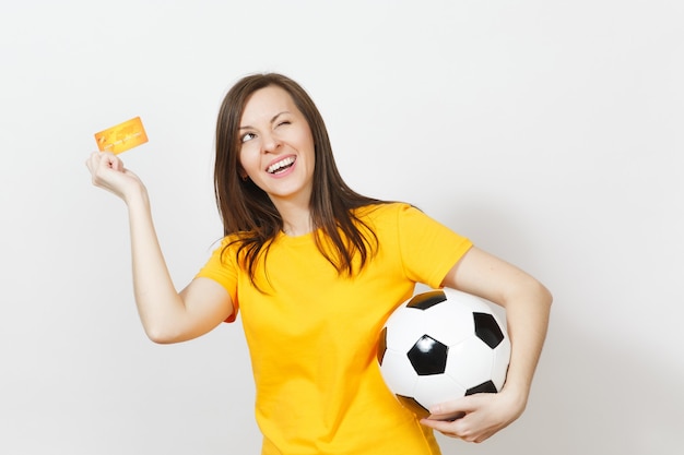 Hermosa joven alegre europea, aficionado al fútbol o jugador en uniforme amarillo con tarjeta de crédito balón de fútbol aislado sobre fondo blanco. Deporte, juego de fútbol, concepto de estilo de vida emocionante.