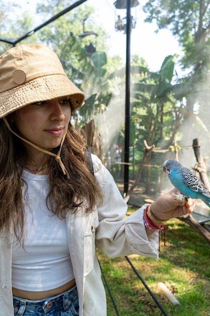 Hermosa joven alimentando a un pájaro con un palo de madera con semillas pegadas a él, el pájaro se detiene para comer