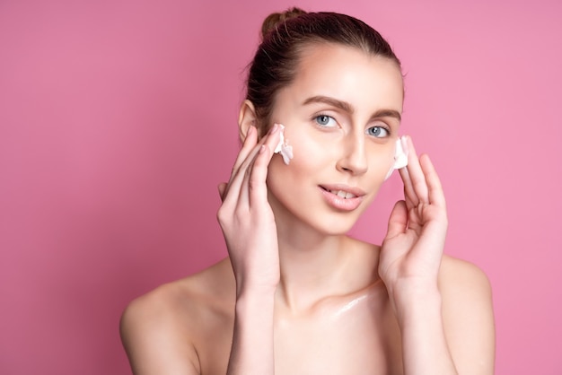 Hermosa joven aplicando crema en el rostro en rosa