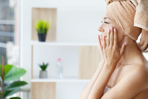 Hermosa joven aplicando mascarilla exfoliante facial en la piel.