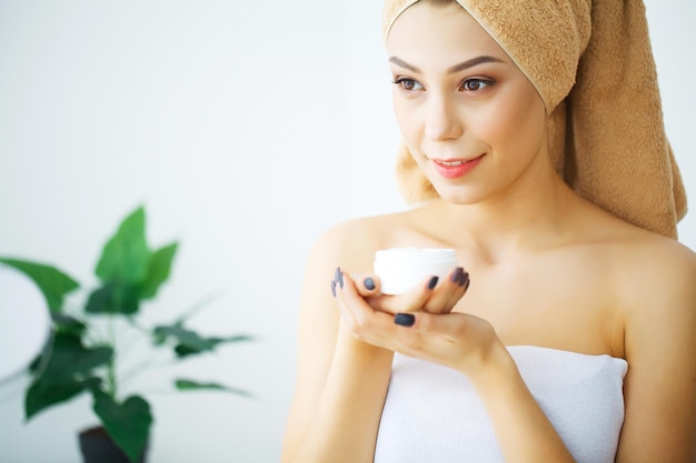 Hermosa joven aplicando el tratamiento de crema cosmética en su rostro