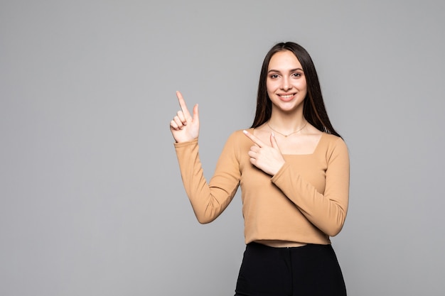 Hermosa joven apuntando hacia arriba, aislado sobre una pared gris