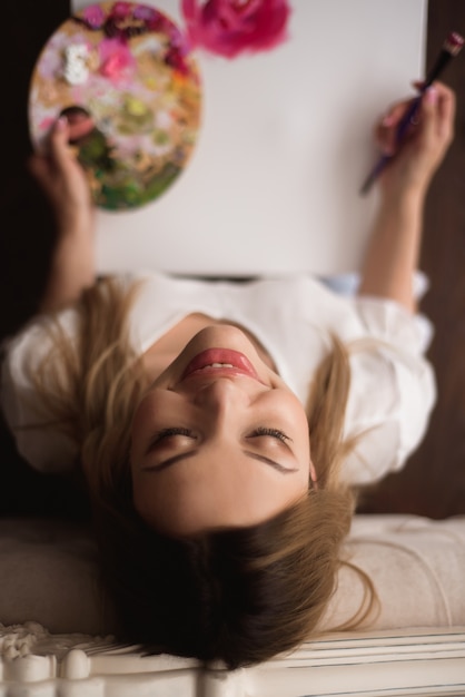 Foto hermosa joven artista pintando en casa peonías rosas