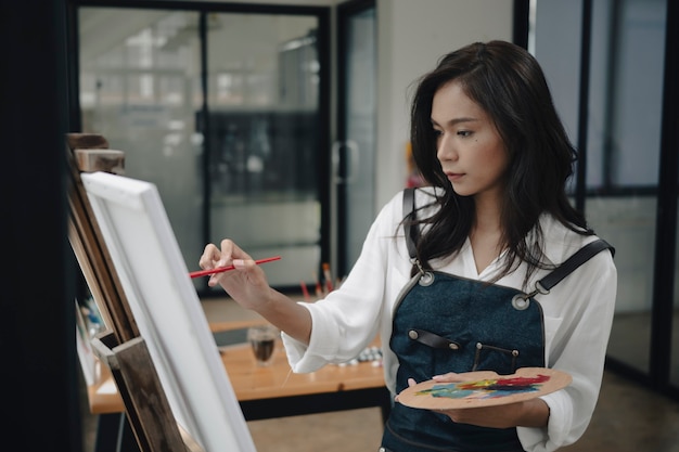 Hermosa joven artista pintando en estudio de arte con acuarela sobre lienzo.