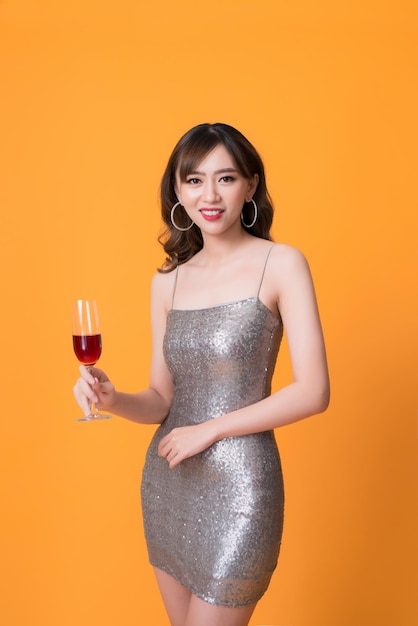 Hermosa joven asiática bebiendo champán en la fiesta sobre fondo amarillo