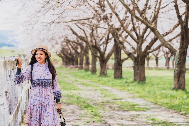 Hermosa joven asiática caminando y tomando fotos en un jardín de hierba verde con sakura y cerezos en flor paisaje de fondo Concepto de viaje en la temporada de primavera de Japón