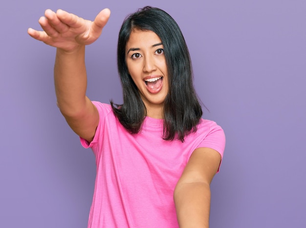 Hermosa joven asiática con una camiseta rosa casual mirando a la cámara sonriendo con los brazos abiertos para un abrazo. expresión alegre abrazando la felicidad.