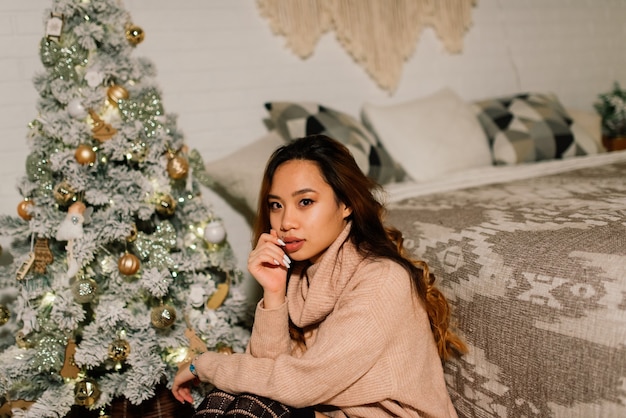 Hermosa joven asiática celebrando la Navidad en casa, divirtiéndose mientras abre regalos