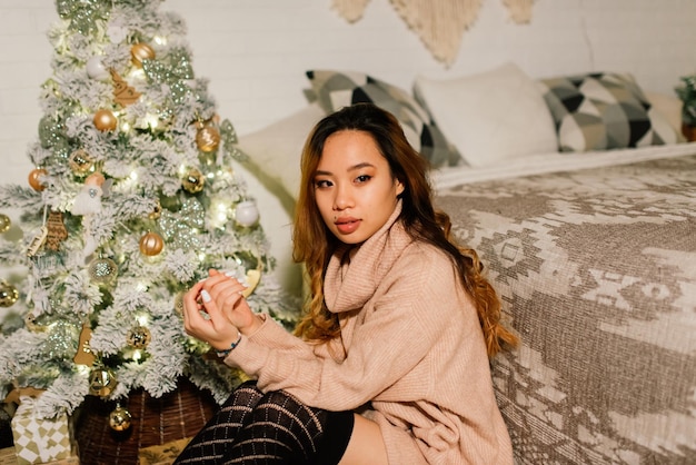 Hermosa joven asiática celebrando la Navidad en casa, divirtiéndose mientras abre regalos