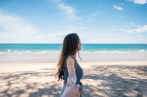 Hermosa joven asiática cogidos de la mano con su novio en la playa de mar tropical en vacaciones