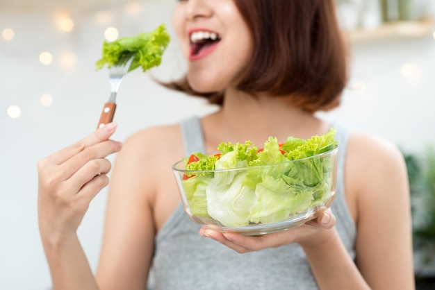 Hermosa joven asiática comiendo ensalada. sonriente niña feliz comiendo alimentos saludables.