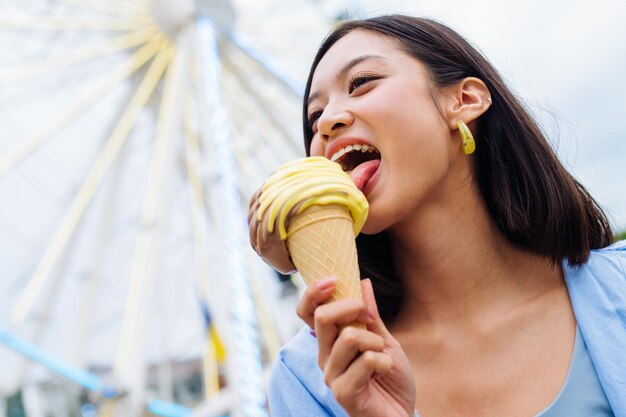 Hermosa joven asiática comiendo helado en el parque de atracciones