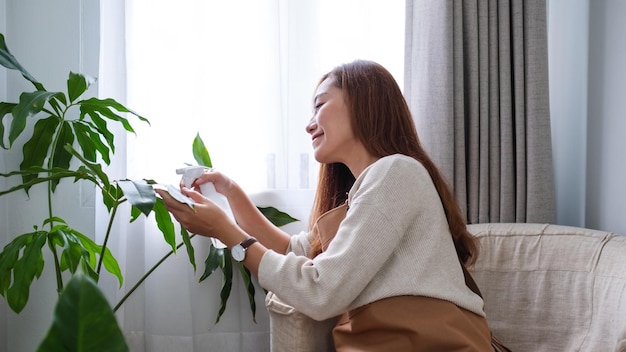 Una hermosa joven asiática cuidando y regando las plantas de interior con una botella de spray en casa