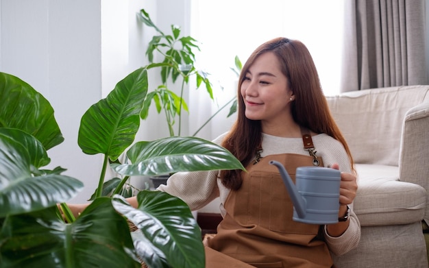 Una hermosa joven asiática cuidando y regando plantas de interior con una lata de agua en casa