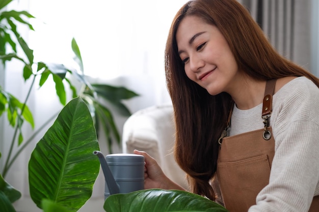 Una hermosa joven asiática cuidando y regando plantas de interior con una lata de agua en casa
