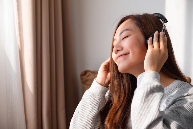 Una hermosa joven asiática disfruta escuchando música con auriculares en casa conceptos de felicidad y relajación