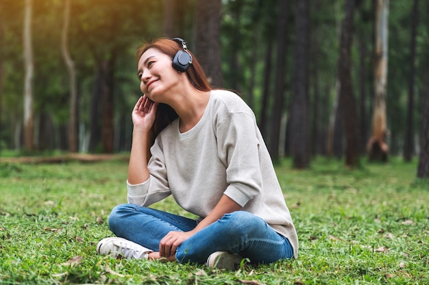 Una hermosa joven asiática disfruta escuchando música con auriculares sintiéndose feliz y relajada en el parque