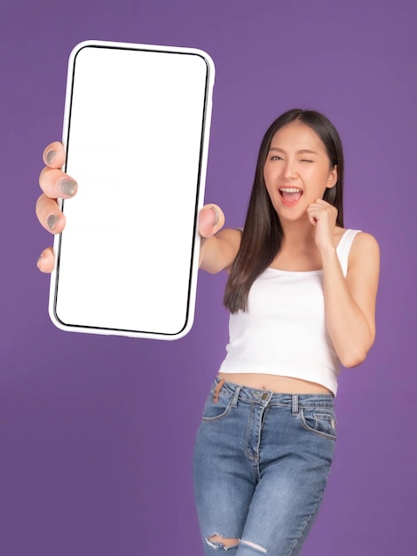 hermosa joven asiática excitada chica sorprendida mostrando un gran teléfono inteligente con pantalla en blanco pantalla blanca aislada en fondo púrpura Mock Up Image