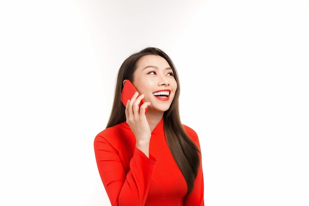 Hermosa joven asiática hablando por teléfono con alguien mientras usa Ao Dai rojo. Aislado en blanco