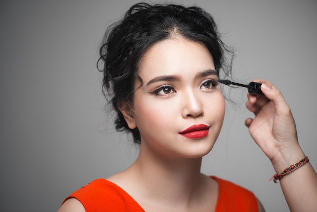 Hermosa joven asiática haciendo maquillaje con rímel en sus pestañas