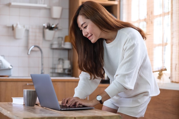 Una hermosa joven asiática independiente que usa una computadora portátil para trabajar en línea en casa