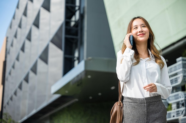 Hermosa joven asiática llamando y hablando por teléfono o teléfono móvil en la ciudad