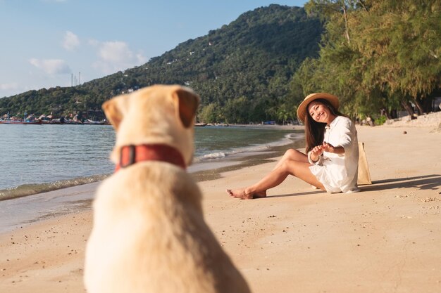 Una hermosa joven asiática llamando y jugando con un perro en la playa