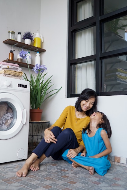 Hermosa joven asiática madre e hija esperando que la lavadora de ropa termine de girar