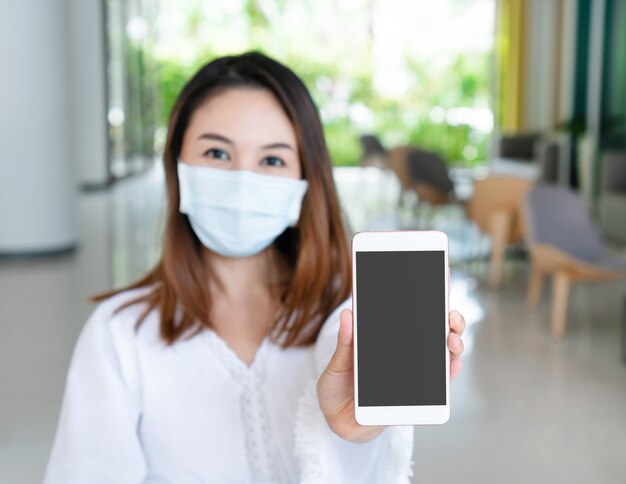 Hermosa joven asiática con mascarilla protectora con smartphone