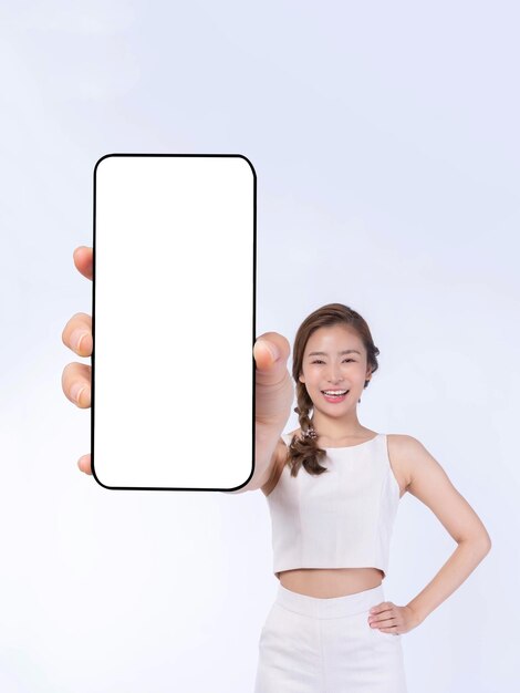 Hermosa joven asiática mostrando un gran teléfono inteligente con pantalla en blanco, pantalla blanca, espacio de copia vacío para banner publicitario aislado en fondo blanco, imagen simulada