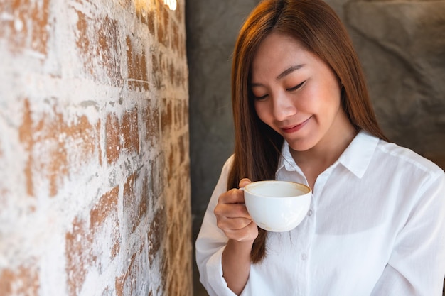 Una hermosa joven asiática oliendo y bebiendo café en la cafetería
