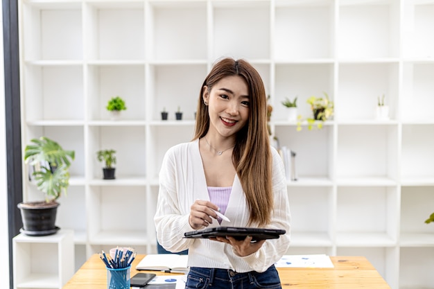 Hermosa joven asiática de pie con tableta en la oficina, imagen de concepto de mujer de negocios asiática trabajando inteligente, ejecutiva moderna, mujer de negocios de inicio, líder empresarial.