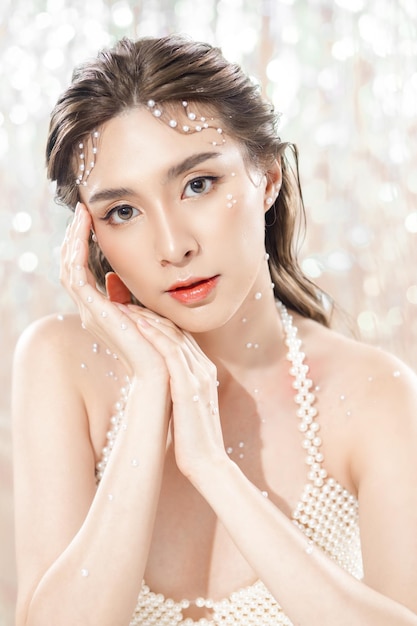 Hermosa joven asiática con piel limpia y fresca con perlas sobre fondo brillante