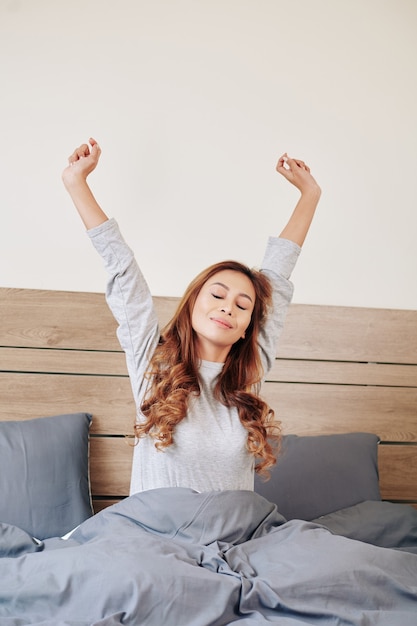 Hermosa joven asiática que se extiende en la cama después de despertarse por la mañana