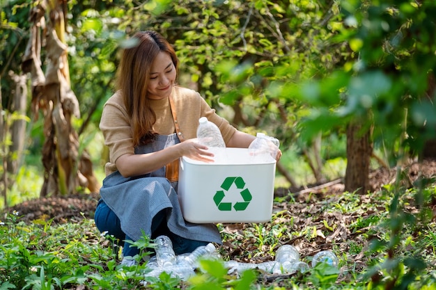 Foto una hermosa joven asiática recogiendo y poniendo botellas de plástico en una papelera de reciclaje al aire libre