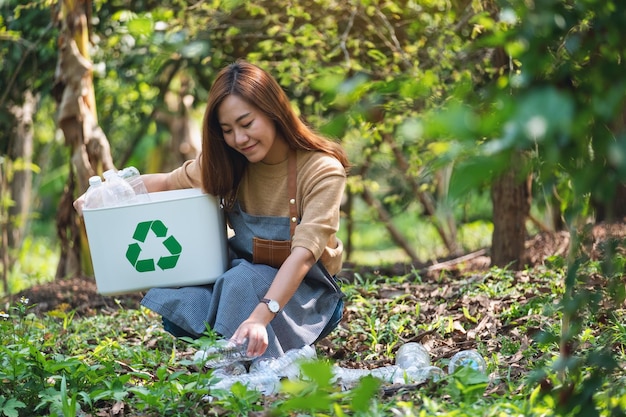 Una hermosa joven asiática recogiendo y poniendo botellas de plástico en una papelera de reciclaje al aire libre