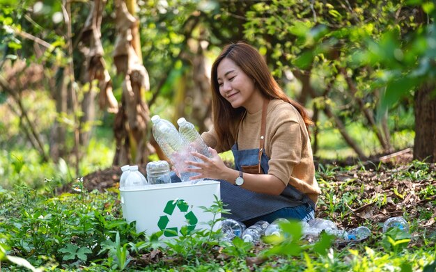 Una hermosa joven asiática recogiendo y poniendo botellas de plástico en una papelera de reciclaje al aire libre