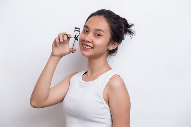 Hermosa joven asiática con rizador de pestañas aislado sobre fondo blanco.